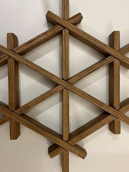 A close-up of a hexagonal Kumiko pattern made from teak wood. This is a more complex pattern that interlocks multiple pieces at different angles to create a snowflake-like design.