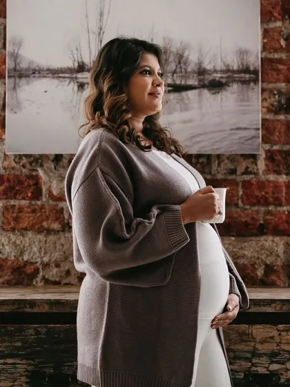A beautiful candid moment. The mom-to-be looks radiant and serene, with a natural makeup look that complements the cozy, indoor setting.