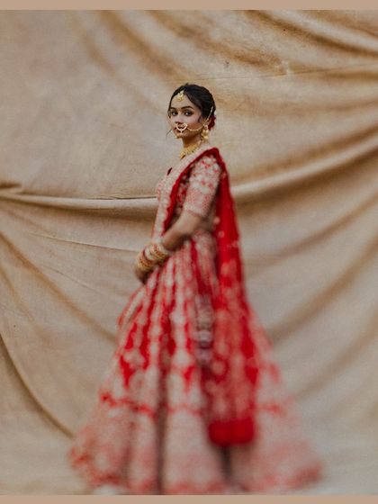 A soft-focus portrait of the bride in her vibrant red lehenga. The artistic blur gives the image a dreamy, painterly quality, focusing on the color and form of her attire.