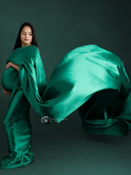 An artistic shot using a flowing green satin fabric to create a dynamic and abstract shape around the mom-to-be.
