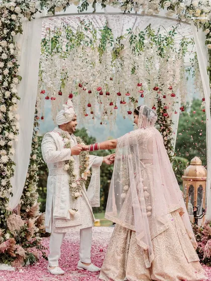 The Varmala exchange under a beautiful floral arch at a mountain wedding. The soft light and petal shower create a romantic and dreamy atmosphere for this key moment.