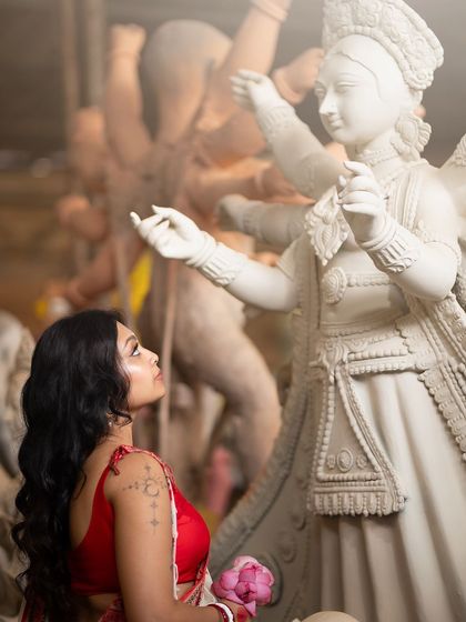 A moment of reverence. The model's side profile shows the soft, glowing makeup against the beautiful backdrop of the Durga idols being made.