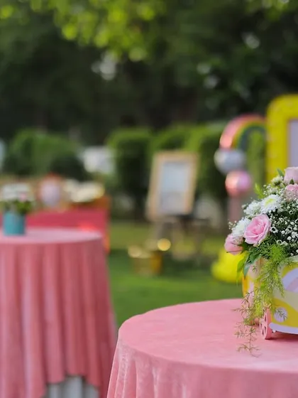 A row of beautifully decorated cocktail tables at the garden party. The pink velvet tablecloths and themed floral centerpieces create a cohesive and elegant look.