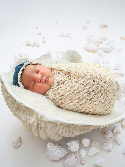A pearl from the ocean. This creative portrait features a baby sleeping inside a large seashell prop, surrounded by smaller shells.