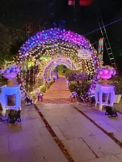 A fairytale entrance tunnel for an evening event. The arch is covered in flowers and illuminated with purple and blue lights, creating a magical and immersive pathway for guests.