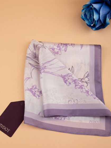 The lavender pocket square folded and styled with a brand tag and a blue rose.