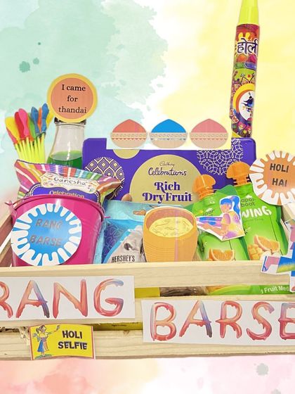 A colourful 'Rang Barse' hamper for Holi. This wooden crate is loaded with snacks, thandai mix, water guns (pichkari), and organic colours for a fun and safe celebration.