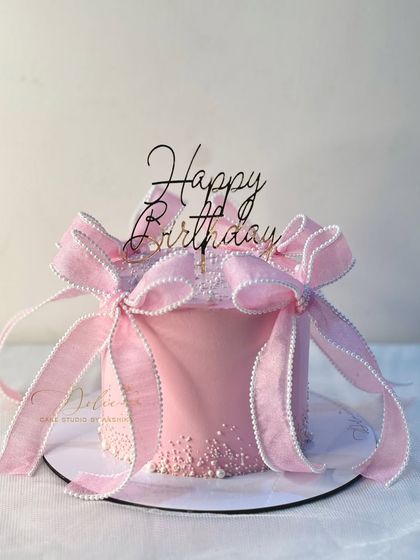 This pink birthday cake features two delicate, handcrafted bows, adding a touch of whimsy and elegance.