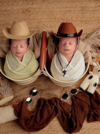 A fun cowboy-themed shoot featuring newborn twins, each wearing a tiny cowboy hat and sleeping in separate bowls on a rustic backdrop.
