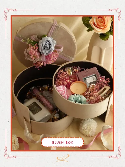 The 'Blush Box' is a sophisticated choice, with two round boxes filled with delicate items like perfumes, scrunchies, and floral arrangements. Its elegant presentation is ideal for someone who loves subtle luxury.