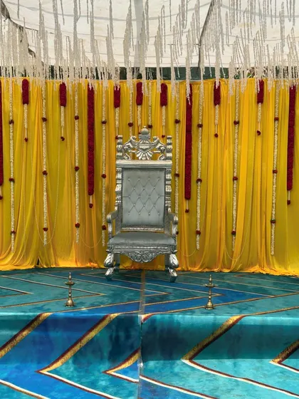 Another perspective of the regal outdoor stage, focusing on the throne and the elegant floral tassels hanging against the yellow backdrop. We can customize these setups anywhere in Karnataka.