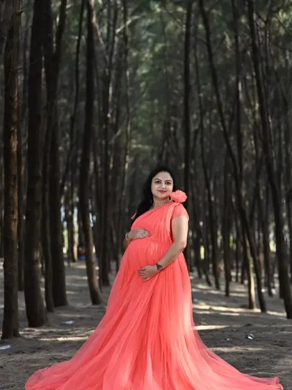 The contrast of this bright coral net gown against the dark woods creates a striking, fairytale-like image. The long trail adds to the enchanting effect.