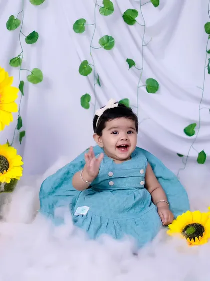 A joyful baby girl waving at the camera during her sunflower-themed sitter session.