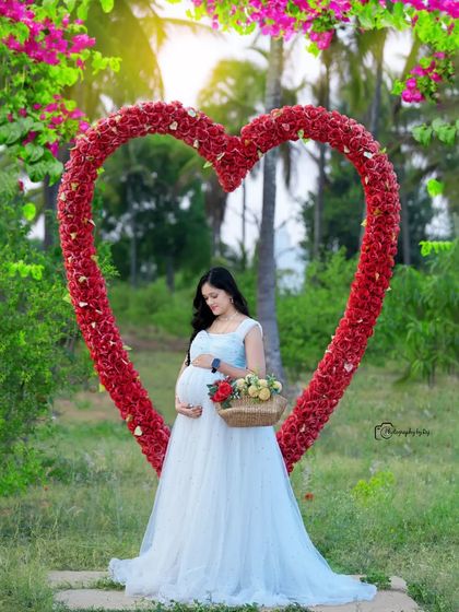 A solo portrait in a light blue gown, framed by our red floral heart prop and holding a basket of flowers.