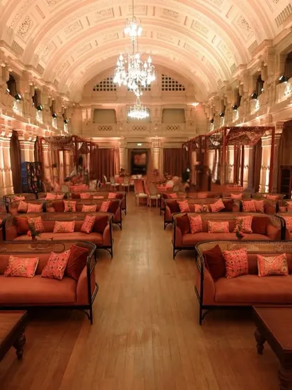 A wide view of the grand hall, filled with elegant lounge seating in warm terracotta tones, all under the magnificent arched ceiling and chandeliers of the palace.