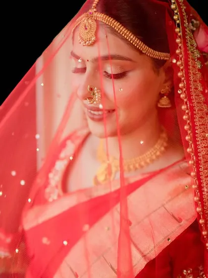 The magic of a classic red bridal look. This shot captures the soft, radiant makeup under a delicate red veil, highlighting a gentle glow and a timeless lip color perfect for the wedding ceremony.
