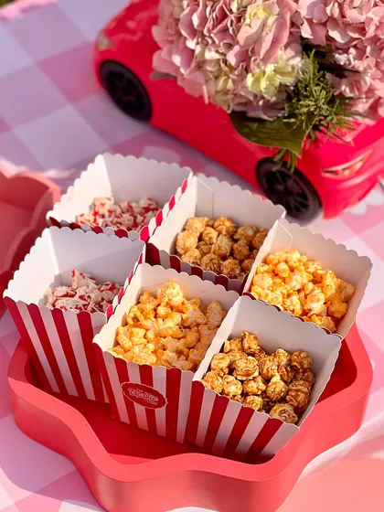 A fun mix of gourmet popcorn flavors served in classic red-and-white striped boxes, perfect for both kids and adults at the Barbie-themed celebration.