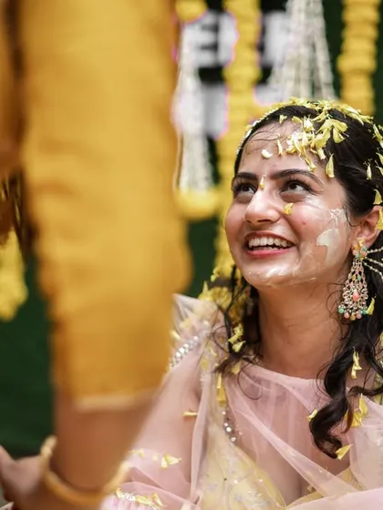 A candid moment of the bride, smiling and covered in haldi, looking at her family.