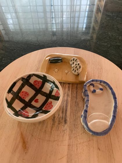 A collection of whimsical pieces from our "Paint-A-Pot" workshop. A student created a miniature couch, a swimming pool trinket dish, and a heart-patterned bowl, each piece a small world of its own.