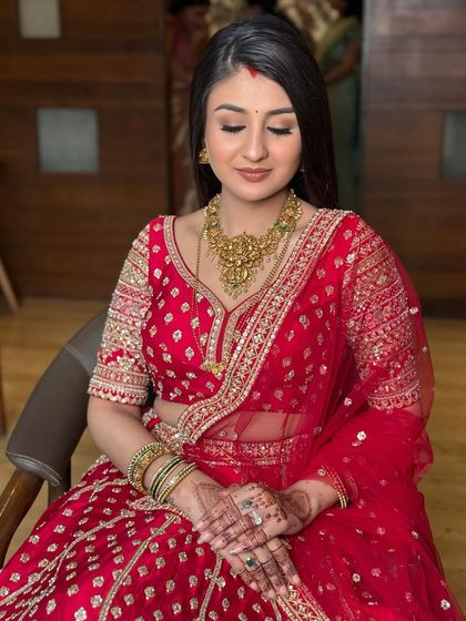A serene portrait of the bride for her reception. Her makeup is soft and luminous, with a focus on flawless skin and subtly defined eyes, paired with a traditional gold necklace.