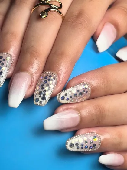 A close-up view of the stone-covered accent nails against a bright blue background, making the sparkle pop.