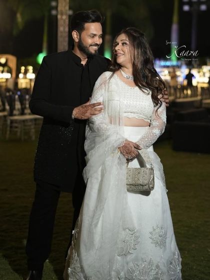A beautiful couple moment. We designed this elegant white lehenga with delicate floral embroidery for her and a classic black Indo-Western kurta set for him, creating a timeless look for their special evening.