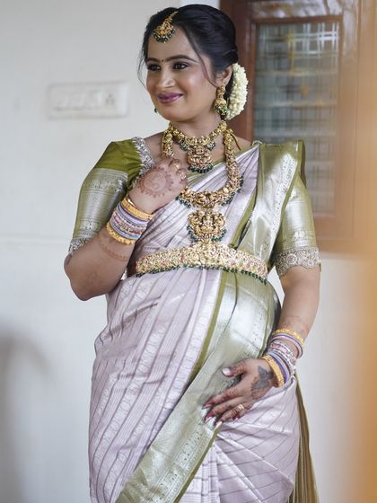 Sushma glowing at her Seemantham. Her look is a perfect example of traditional elegance, with a soft green and silver saree, layered temple jewelry, and a fresh, dewy makeup finish.