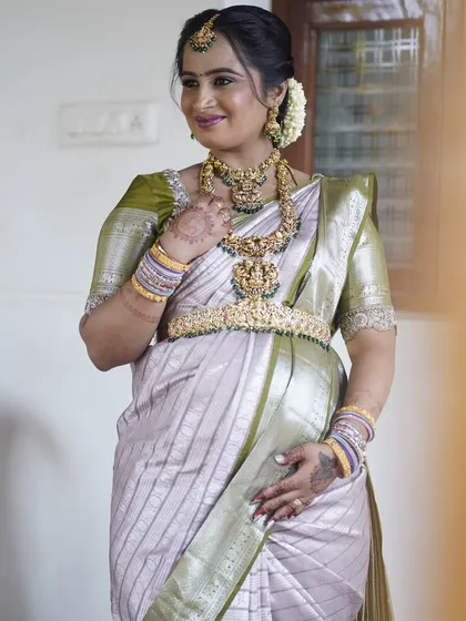 Sushma glowing at her Seemantham. Her look is a perfect example of traditional elegance, with a soft green and silver saree, layered temple jewelry, and a fresh, dewy makeup finish.