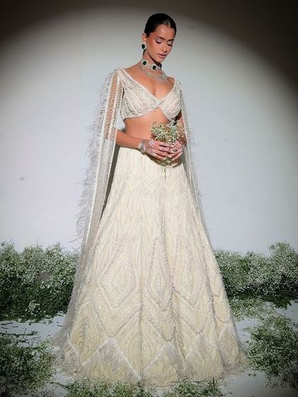 An ivory lehenga embellished with delicate pearls and intricate craftsmanship, paired with a blouse featuring dramatic feathered sleeves.