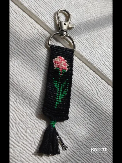 This knotted keychain features a delicate pink flower design on a black background. It’s an elegant and subtle floral accessory.