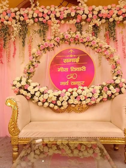 A close-up of a beautiful Sagai stage, showing the custom name sign surrounded by a ring of pink and white roses over a classic white and gold sofa.
