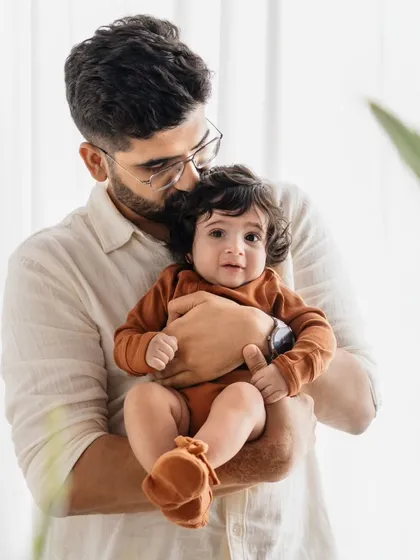 A father holds his baby boy close. The soft, natural light from the window creates a serene and loving mood for this portrait.