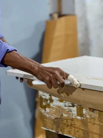 The final touches are applied by hand. Here, a worker is carefully applying adhesive for edge banding, a crucial step for a seamless and durable finish.