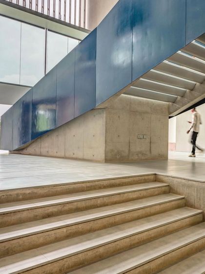 The underside of a grand staircase at the JSW School of Public Policy reveals its structural logic. The blue steel cladding contrasts with the raw concrete, highlighting the different material components of the design.