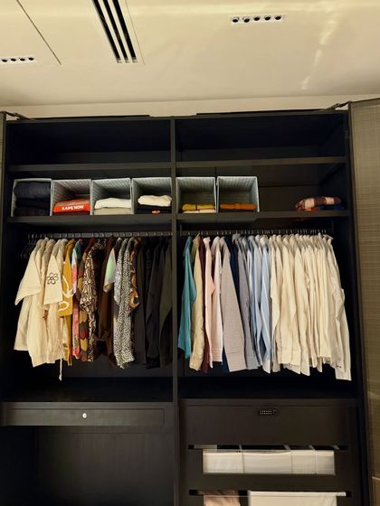 A sleek, modern wardrobe in a dark finish that we organized. We used light-colored bins on the top shelf for contrast and visibility, ensuring that even items stored up high are easy to identify and access.