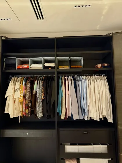 A dark wood wardrobe organized for a gentleman. We've separated casual, colorful shirts from formal button-downs, with folded items stored neatly in bins on the shelves above and below.