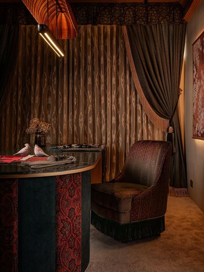 A close-up of the custom swivel chair and the fabric-paneled client table. The rich, embroidered fabric of the chair complements the alternating red and teal panels of the table, showcasing our bold use of color and pattern.