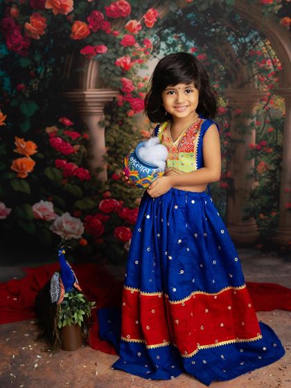 Our little Radha, holding her pot of butter with a sweet smile. The colorful lehenga and floral background bring the Janmashtami theme to life.