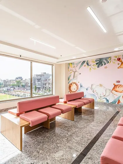 This pediatric waiting area at Sarvesh Health City features a large window for natural light and a charming wall mural. The comfortable, low-to-the-ground seating is scaled for children and their families.