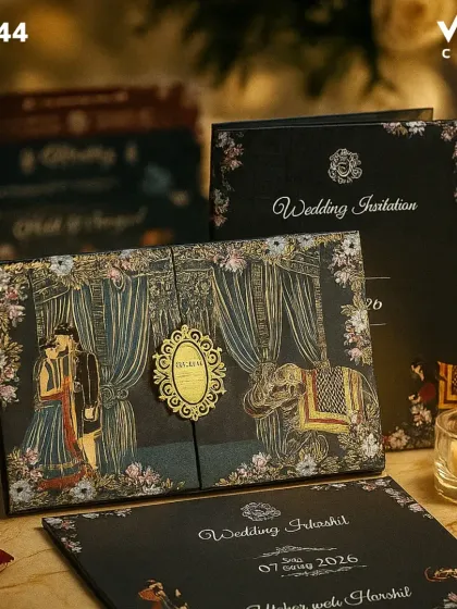 This is a premium boxed invitation designed for a grand wedding. The dark, elegant background makes the gold foil illustrations of the couple, wedding canopy, and elephants stand out. The intricate detailing makes it a true statement piece.