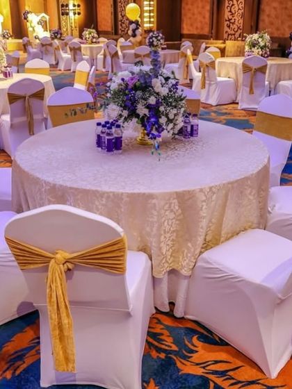 The guest seating at the royal prince party. Tables are dressed in elegant lace cloths with gold chair sashes, and feature beautiful purple and white floral centerpieces.