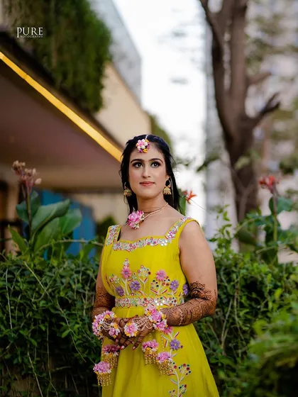 A stunning portrait of the bride at her Mehndi ceremony. Her bright yellow dress and pink floral jewelry create a beautiful, fresh look.