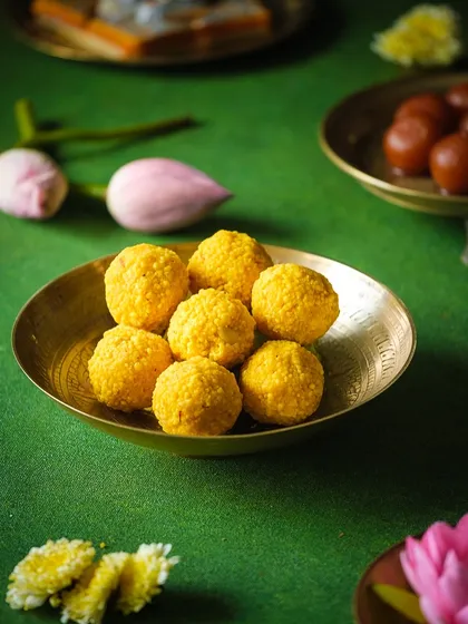 A beautifully styled shot of laddoos in a brass bowl, surrounded by flowers. This demonstrates classic food styling principles for traditional Indian sweets.