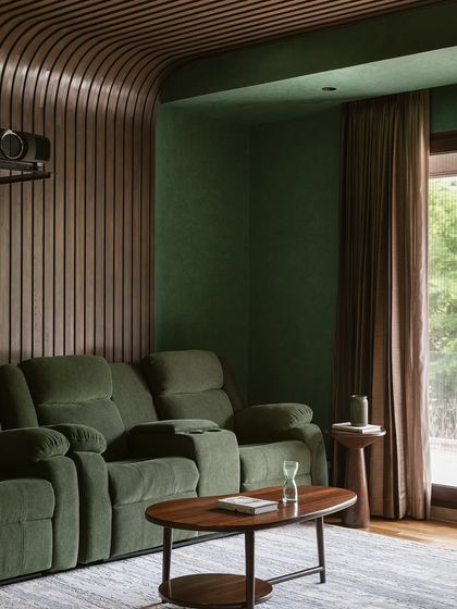 A different angle of the media room, showing the deep green walls and heavy blackout curtains that create an immersive viewing experience. The space is both functional and highly stylized.