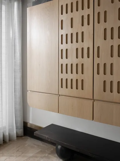 A custom floating shoe cabinet with a unique perforated pattern on the doors, paired with a minimalist black bench. This piece combines modern design with practical storage.