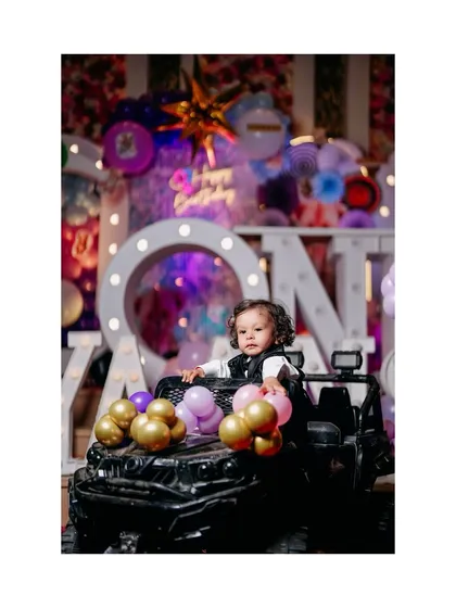 A little boy enjoying his birthday party from the driver's seat of a toy jeep. The balloons add a festive touch to this fun, candid shot.