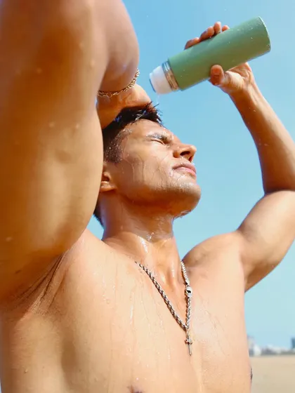 A creative product placement shot. The model pouring water on himself from a bottle creates a refreshing, high-summer feel. This type of shot is perfect for advertising drinks, skincare, or accessories in a lifestyle context.