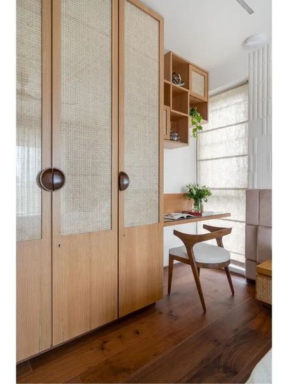 Functionality meets warmth in this corner of the parents' bedroom. A custom wardrobe with cane-panelled doors provides ample storage, while a compact wooden desk creates a small, light-filled study area by the window.