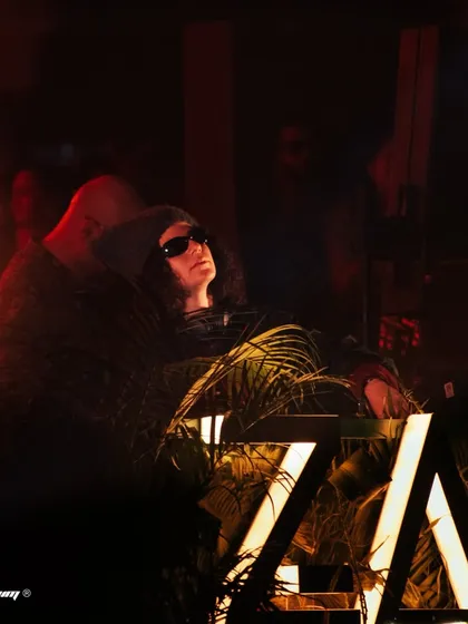Carlita at her decks, surrounded by plants and bathed in warm, moody lighting at Zamna Festival.
