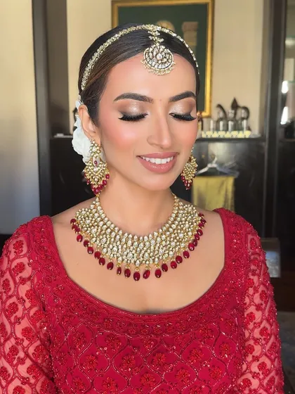 A close-up with eyes closed, highlighting the soft and shimmering eyeshadow work that adds a touch of glamour to her classic red bridal look.